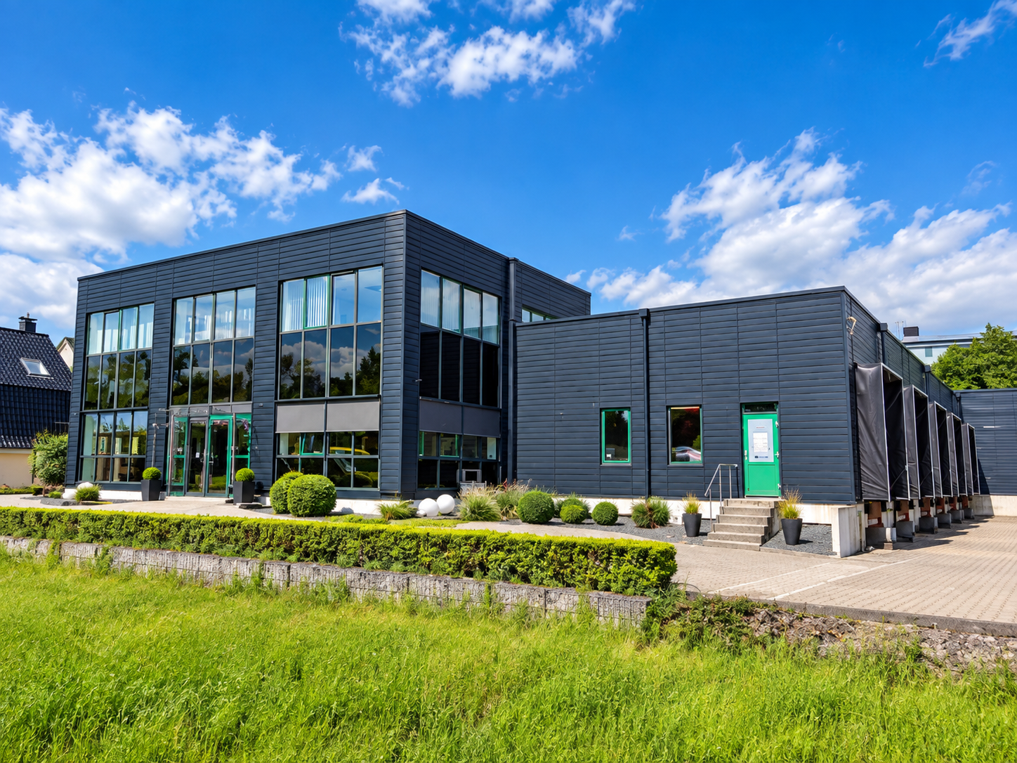 Gewerbehalle mit dunkler Fassade, großer Verglasung und begrüntem Vorbereich